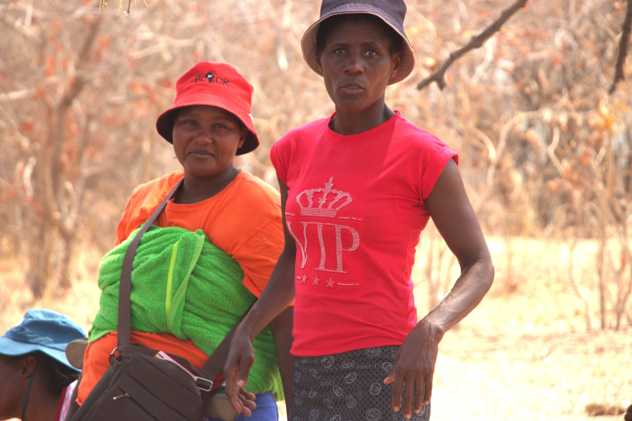 Two women walking in a flood-prone community in Harare, one carrying a baby on her back, illustrating the impact of climate change on maternal health and daily life