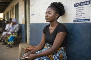 A young Zimbabwean woman seated outside a clinic looking thoughtful, symbolising access to healthcare, reproductive justice and informed decision-making.